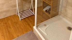 Een douchecel met een glazen deur, een metalen handdoekhouder en een houten plankunit.