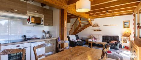 A wooden dining table with chairs, a kitchen with white cabinets and a microwave, a staircase, and a living area with a sofa and a coffee table.