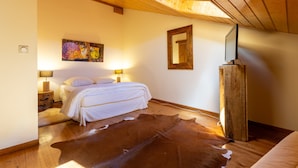 Een slaapkamer met een houten plafond, een bed, een kuitenvacht vloerkleed, een schilderij en een spiegel.