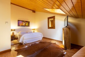 Ein Schlafzimmer mit Holzbalkendecke, einem Bett, einem Kuhfellteppich, einem Gemälde und einem Spiegel.