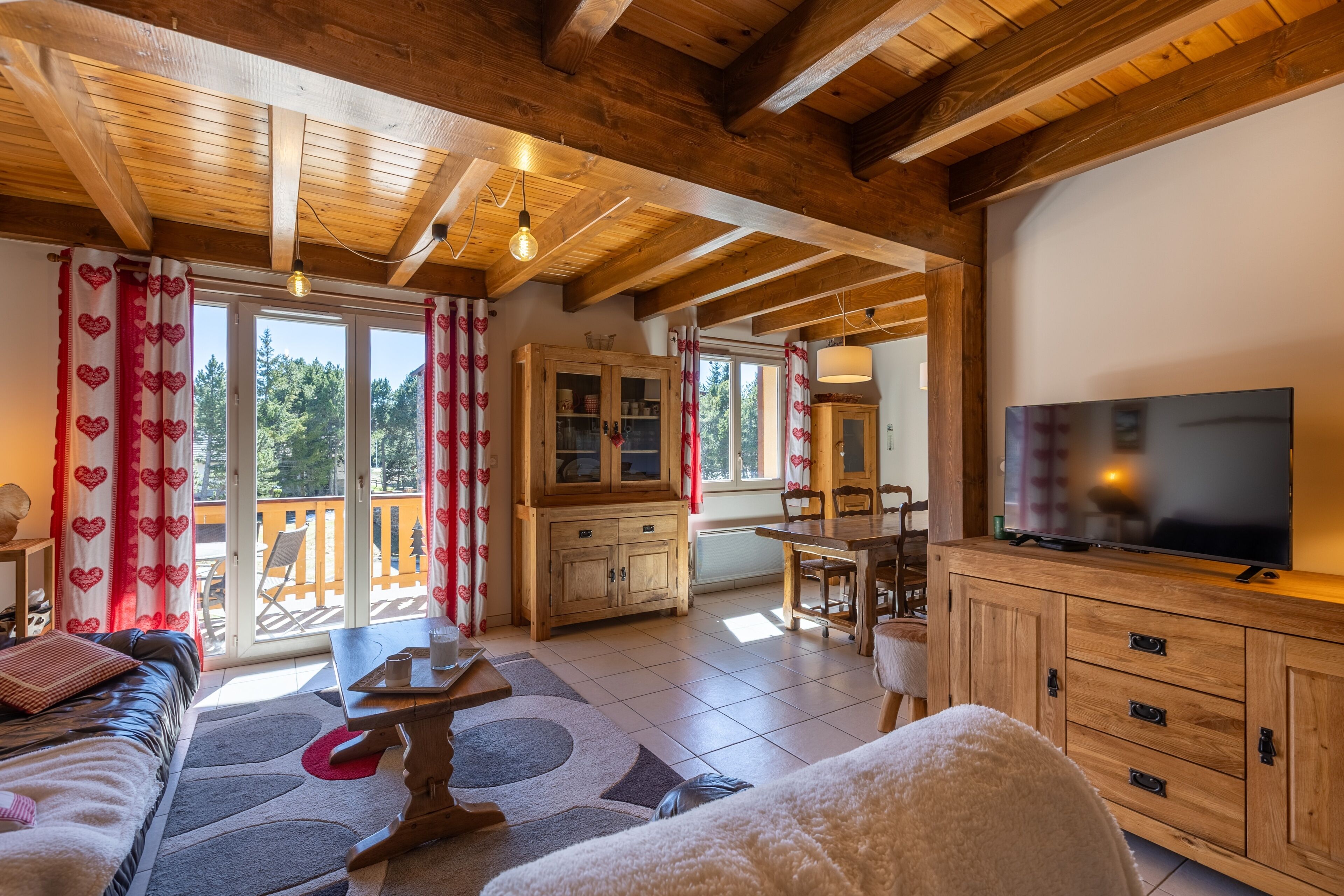 A cozy living room with wooden beams, a television, and a dining area with a table and chairs.
