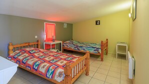 Ein Zimmer mit zwei hölzernen Betten, einem kleinen Tisch, einem Heizkörper und einem Fenster mit rotem Vorhang.