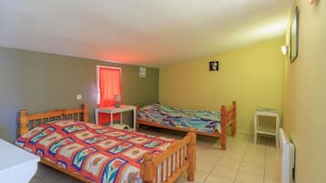 A room with two wooden beds, a small table, a radiator, and a window with a red curtain.