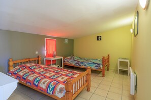 Ein Zimmer mit zwei hölzernen Betten, einem kleinen Tisch, einem Heizkörper und einem Fenster mit rotem Vorhang.