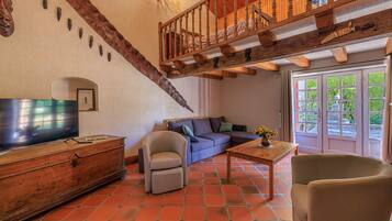Una sala de estar con televisor, sofá, sillón, escalera de madera y vistas a través de un ventanal.