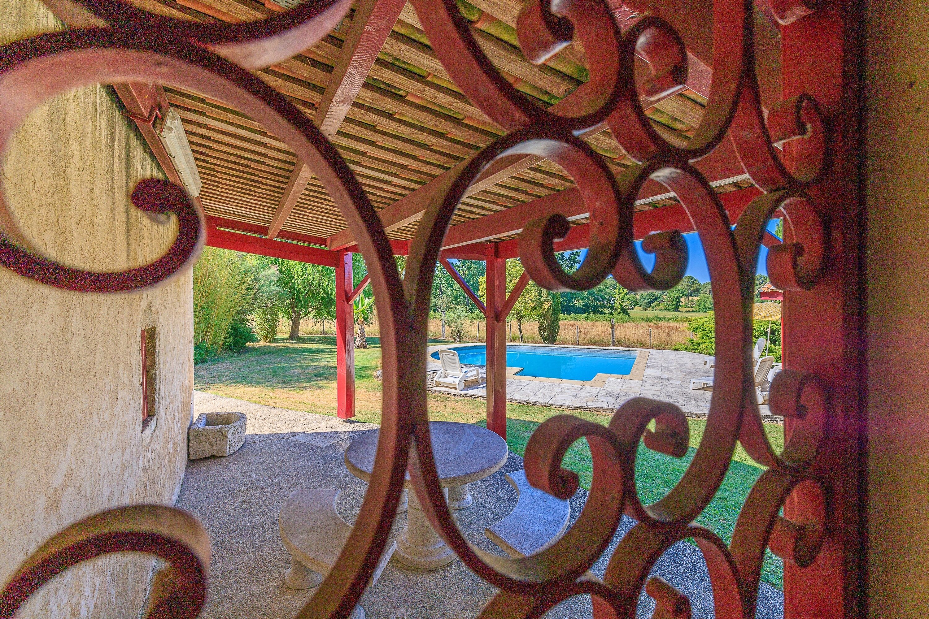 A covered outdoor area with a pool, surrounded by greenery.