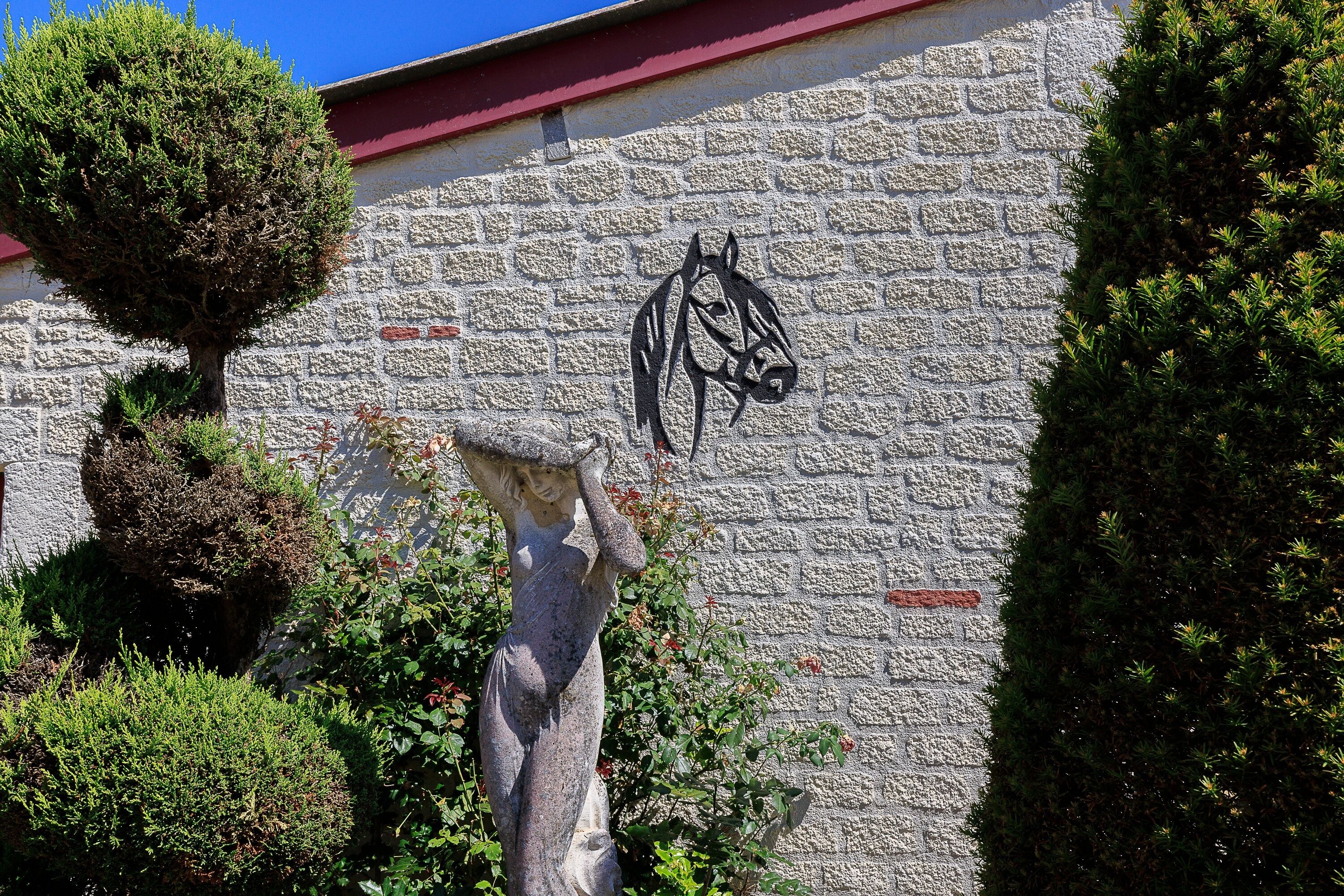 Un muro de piedra con una escultura de caballo y un árbol pequeño.