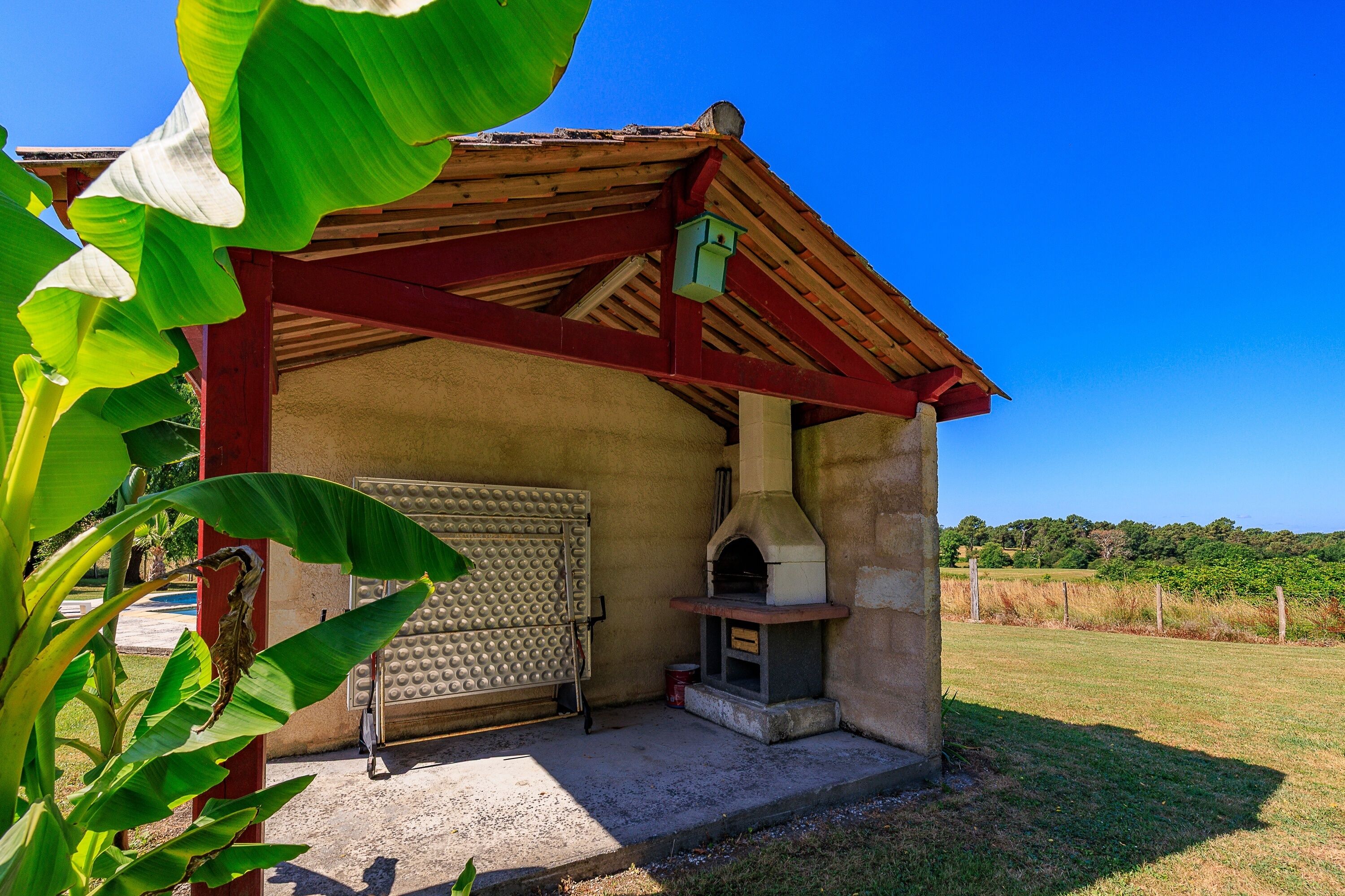 Une petite construction extérieure dotée d’un four en briques, d’un barbecue en métal et d’un toit en bois.