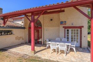 A covered patio with a stone floor, a table with chairs, and a red-framed door.