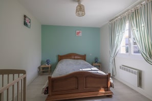 A bedroom with a wooden bed, a nightstand, a lamp, a radiator, and a window with curtains. - Le Colombier de Sauvignac - Avec piscine privée (Sauvignac)