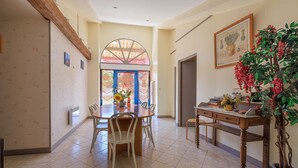 A dining area with a round table, chairs, a potted plant, and a window with a view. - Le Colombier de Sauvignac - Avec piscine privée (Sauvignac)