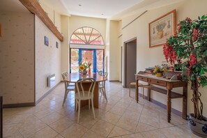 A dining area with a round table, chairs, a potted plant, and a window with a view. - Le Colombier de Sauvignac - Avec piscine privée (Sauvignac)