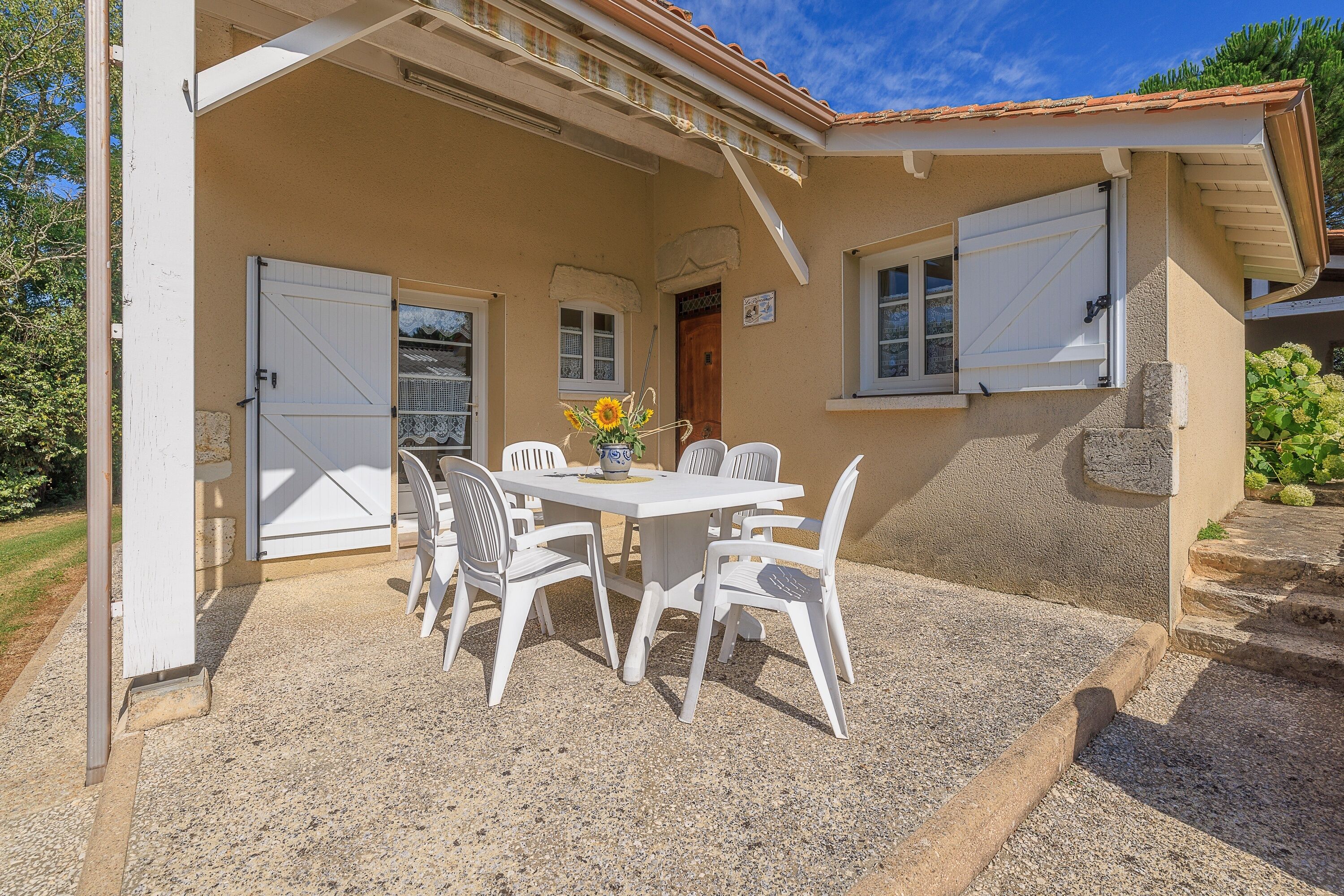 A covered patio with a table and chairs, a door, and a window with shutters.