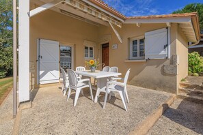 A covered patio with a table and chairs, a door, and a window with shutters. - Le Colombier de Sauvignac - Avec piscine privée (Sauvignac)