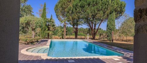 A swimming pool with a curved edge, surrounded by a paved deck and trees.
