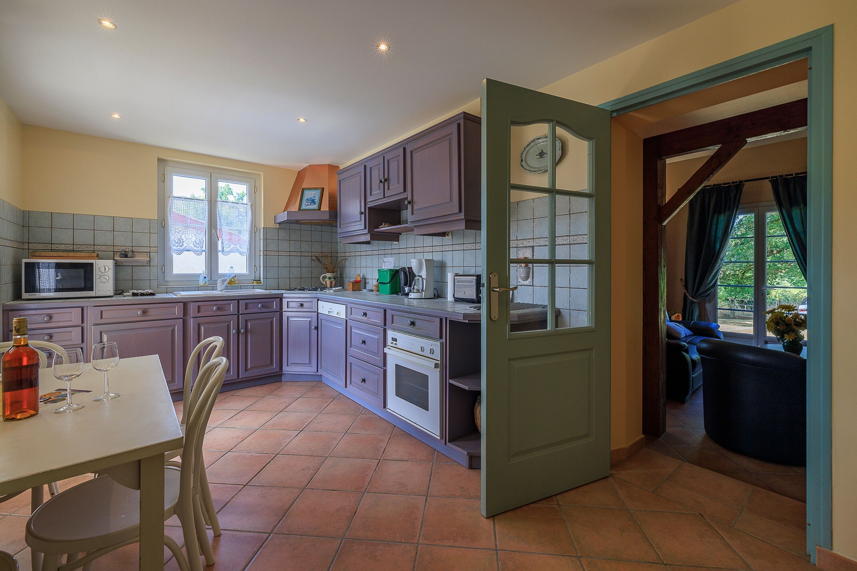 Una cocina con comedor, microondas, estufa y ventana con cortinas de encaje.
