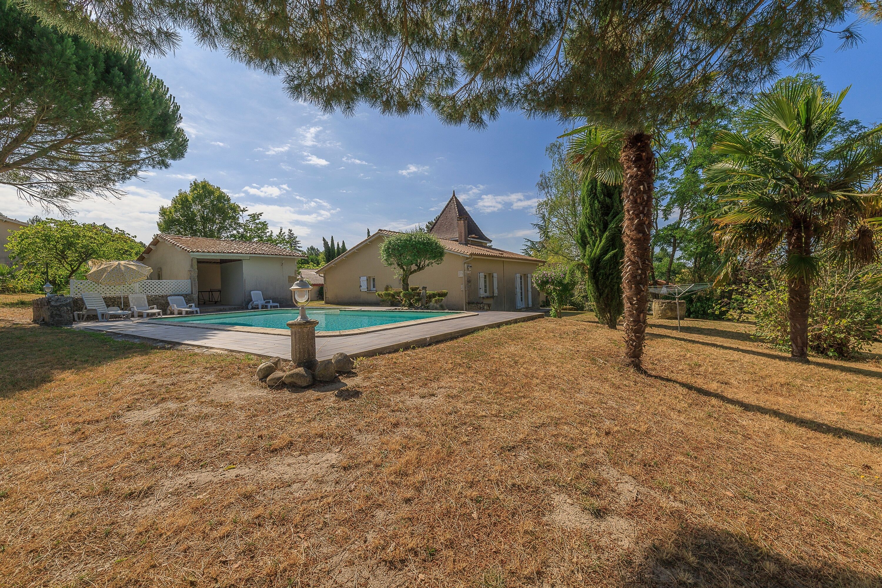 A residential property with a swimming pool, a covered patio area, and a well-maintained lawn.