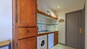 A kitchen with wooden cabinets, a washing machine, a microwave, and a tiled backsplash. - Le Colombier de Sauvignac - Avec piscine privée (Sauvignac)