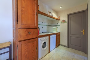 A kitchen with wooden cabinets, a washing machine, a microwave, and a tiled backsplash. - Le Colombier de Sauvignac - Avec piscine privée (Sauvignac)
