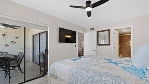 Ein Schlafzimmer mit einem Bett, einem Deckenventilator, einem Fernseher und einer Tür zu einem Badezimmer.