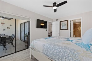 Ein Schlafzimmer mit einem Bett, einem Deckenventilator, einem Fernseher und einer Tür zu einem Badezimmer.