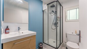 Et badeværelse med glasbrusekabine, en hvid vask, et spejl og et toilet.