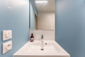 Une salle de bain avec un lavabo blanc, un miroir et un flacon de savon pour les mains.