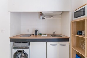 Eine kompakte Küche mit Waschmaschine, Kaffeemaschine und einer Mikrowelle über der Arbeitsfläche.