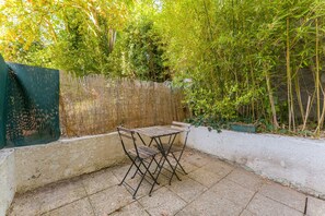 Eine Terrasse mit Tisch und Stühlen, umgeben von einem Bambuszaun und viel Grün.