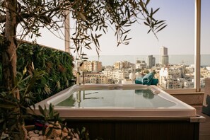 Uma banheira de hidromassagem com vista para a cidade, rodeada por vegetação e um céu limpo.