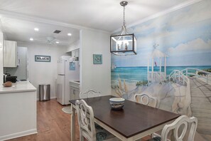 A dining area with a beach mural, white cabinetry, and a modern kitchen in the background. - 2br/2ba Ocean Walk condo for monthly rentals - December through March (Saint Simons Islandd)