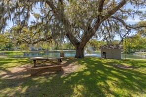 A picnic table under a large tree with hanging moss, a small shed, and a pond in the background. - 2br/2ba Ocean Walk condo for monthly rentals - December through March (Saint Simons Islandd)