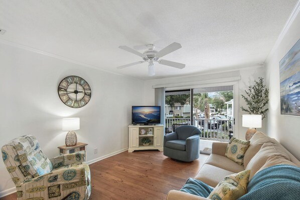 A living room with a ceiling fan, a television, a couch, and a chair. - 2br/2ba Ocean Walk condo for monthly rentals - December through March (Saint Simons Islandd)