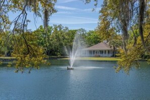 A lake with a fountain, surrounded by trees and a building with a roof. - 2br/2ba Ocean Walk condo for monthly rentals - December through March (Saint Simons Islandd)