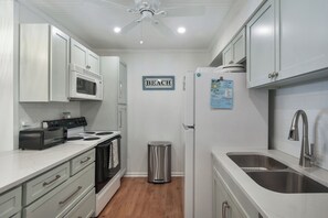 A compact kitchen with white cabinets, a microwave, a stove, a trash bin, and a sink. - 2br/2ba Ocean Walk condo for monthly rentals - December through March (Saint Simons Islandd)