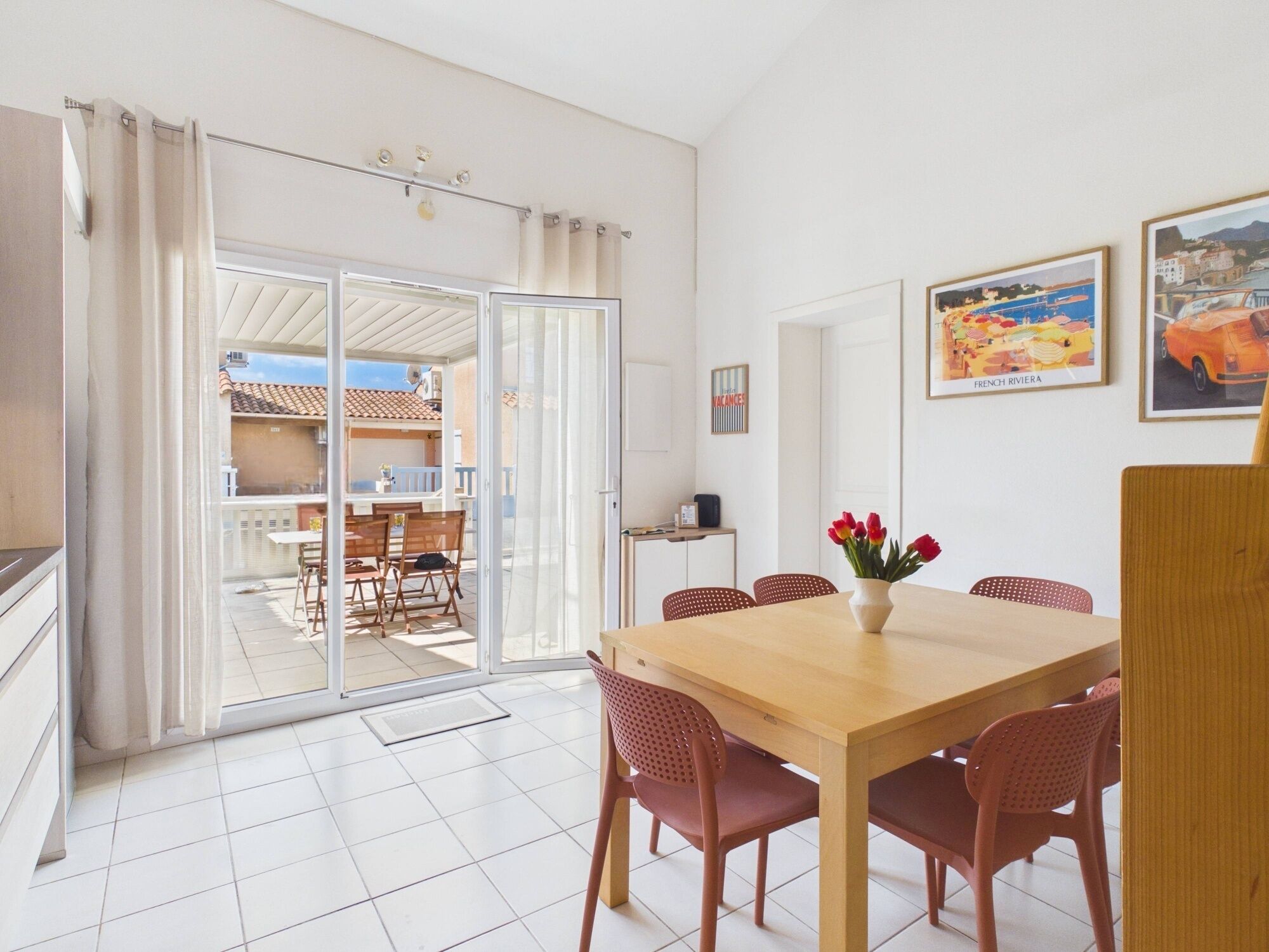 A dining area with a table, chairs, a vase of flowers, and a view through a glass door to an outdoor patio.
