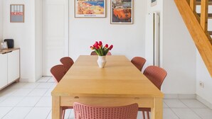 A dining area with a wooden table, red chairs, a vase of tulips, and two framed pictures on the wall. - La Maison L'île Bleue - À 700 m de la plage (Gruissan)
