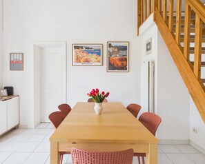 Ein Essbereich mit einem Holztisch, roten Stühlen, einer Tulpenvase und zwei gerahmten Bildern an der Wand.