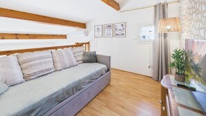 A modern living room with a sofa, wooden beams, a window, and wall art. - La Maison L'île Bleue - À 700 m de la plage (Gruissan)