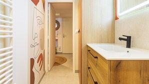 A modern bathroom with a white sink, wooden cabinetry, and a mirror. - Suite Jungle Premium - Studio climatisé (Toulon)