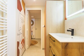 A modern bathroom with a white sink, wooden cabinetry, and a mirror. - Suite Jungle Premium - Studio climatisé (Toulon)