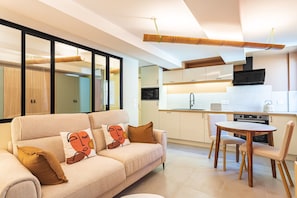 A modern living room with a sofa, a dining table, and a kitchen in the background. - Suite Jungle Premium - Studio climatisé (Toulon)