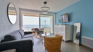 Ein modernes Wohnzimmer mit einer Couch, einem Korbsessel, einem Fernseher und einem Balkon mit Blick.