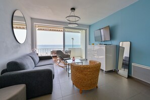 Ein modernes Wohnzimmer mit einer Couch, einem Korbsessel, einem Fernseher und einem Balkon mit Blick.