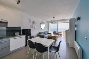 A modern kitchen with white cabinets, a dining table with black chairs, a gray sofa, and a view of the sea through large windows. - La Résidence - Appt avec balcon et vue mer (La Baule)