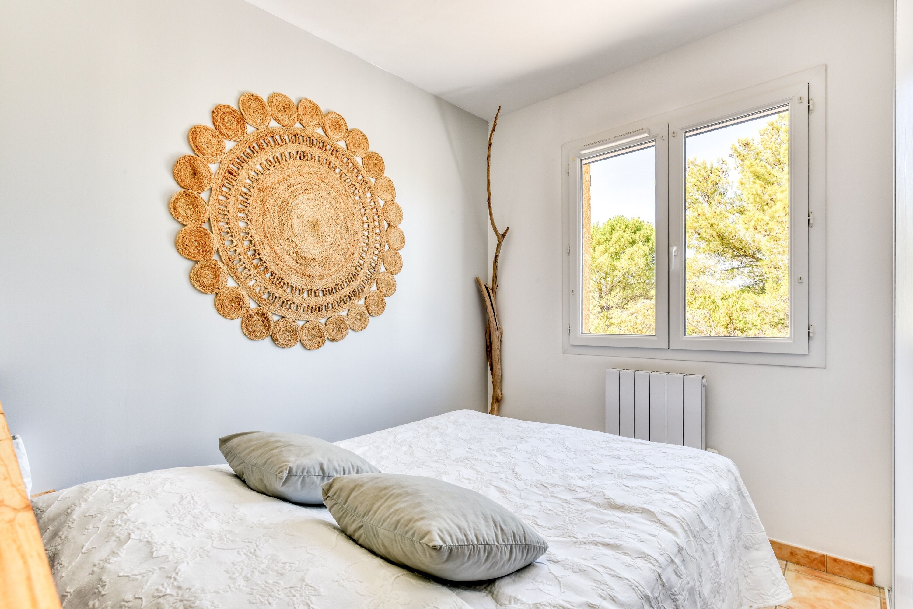 Une chambre à coucher avec un lit, des oreillers, une décoration murale, une fenêtre et un radiateur.