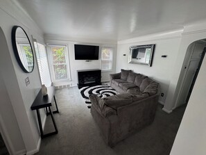 A living room with a grey sofa, a flat-screen TV, a fireplace, and a black and white rug. - Family Vacation house (Redford)