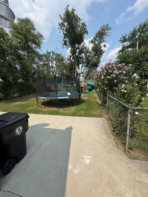 A backyard with a trampoline, a green slide, and a black trash bin. - Family Vacation house (Redford)
