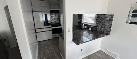 A compact kitchen with white cabinets, a black countertop, and a window with blinds.