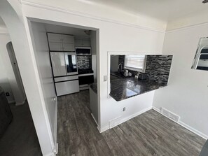 A compact kitchen with white cabinets, a black countertop, and a window with blinds. - Family Vacation house (Redford)